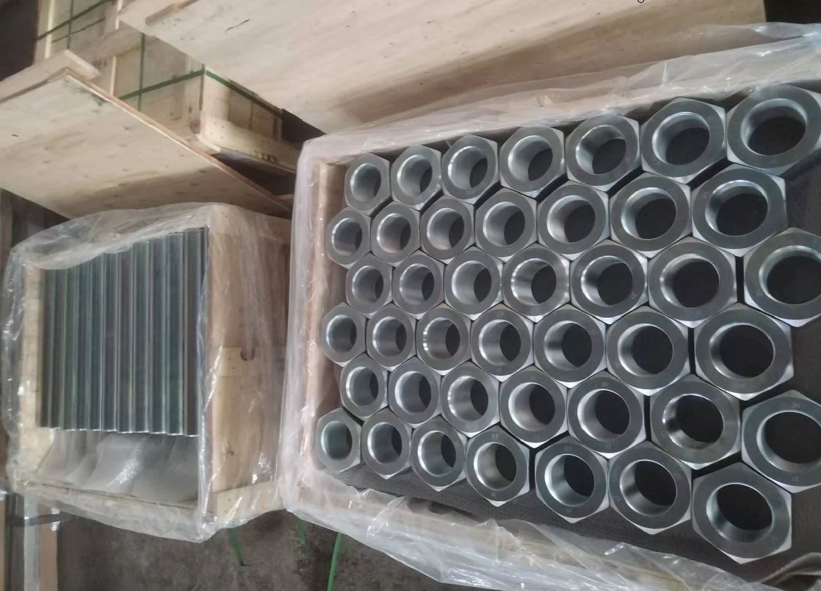 Heavy hex nuts with visible EF and 2H markings packed beside full-thread studs